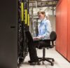 Frau sitzt auf einem Bürostuhl in einem Rechenzentrum und arbeitet am Laptop