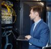 IT Systemadministrator überprüft die IT Infrastruktur an einem Netzwerkschrank mit Laptop