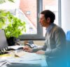 Mann arbeitet an einem Büroarbeitsplatz mit Computer, Telefon und Unterlagen