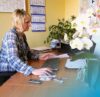 Frau sitzt an einem Schreibtisch und arbeitet mit Maus und Tastatur an einem Büroarbeitsplatz