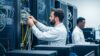 zwei IT-Systemadministratoren arbeiten in einem Serverraum an der Verkabelung