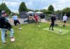 sieben IT-Systemadministratoren stehen im Halbkreis und spielen Fußballgolf bei einem Teamevent
